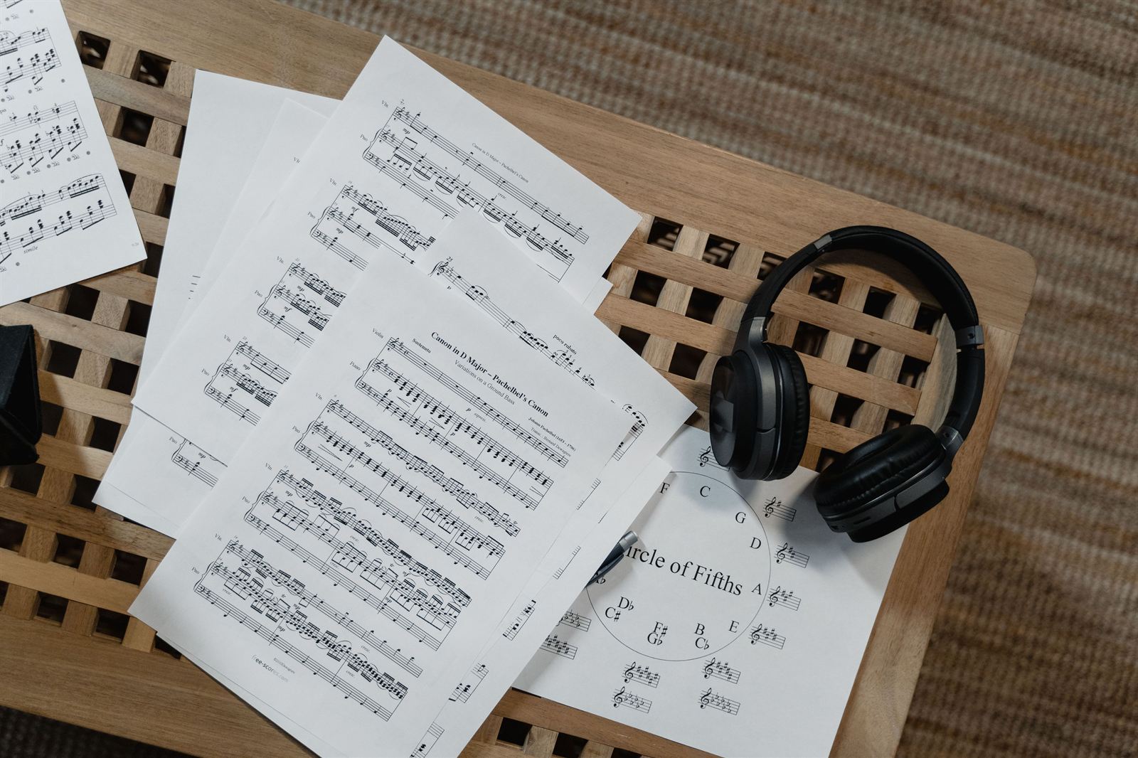 Sheet music and a circle of fifths chart spread across a wooden table next to a pair of black over-ear headphones